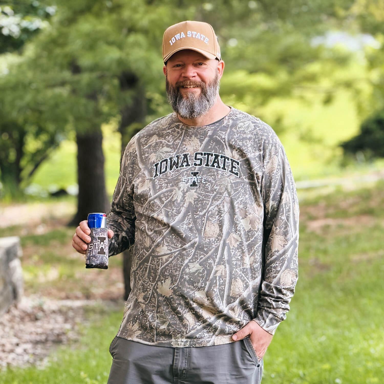 A man wearing an Iowa State Camo t-shirt and hat while holding a camo can cooler.